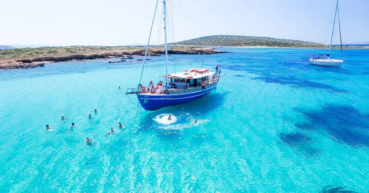 Swimmers in turquoise water beside a white day-cruise boat on a Paros boat tour to Antiparos and Despotiko, Greece