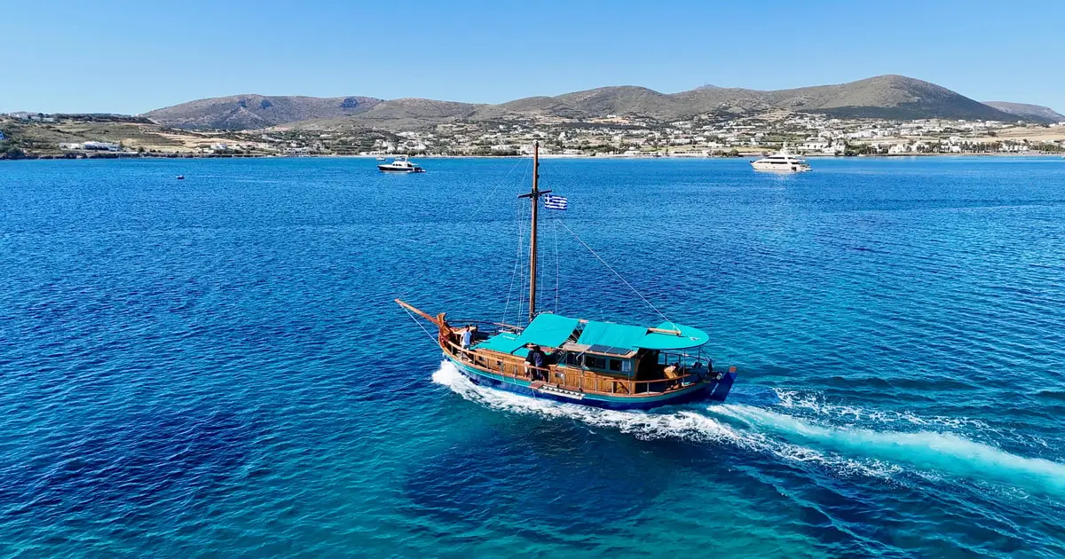 Traditional wooden boat cruising past the granite coves of Kolymbithres beach in Naoussa Bay, Paros